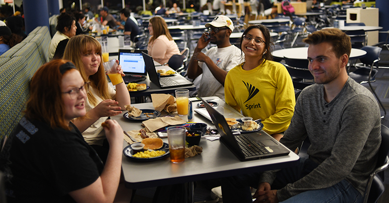 Diverse group of students gathered around a table eating and studying
