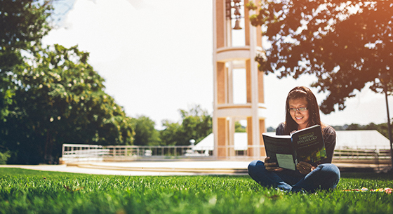 Photo of Hispanic girl reading a book on the bell tower quad