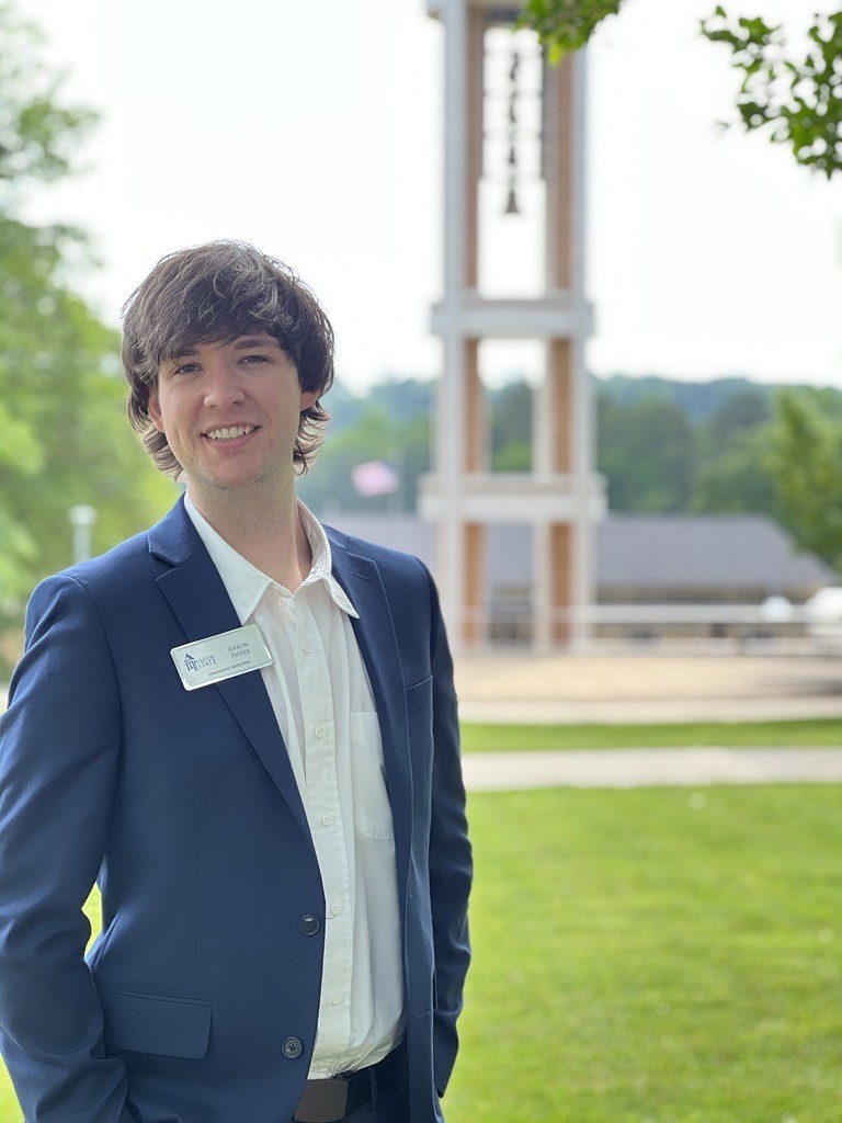 Male in business attire standing in front of Dalton State bell tower