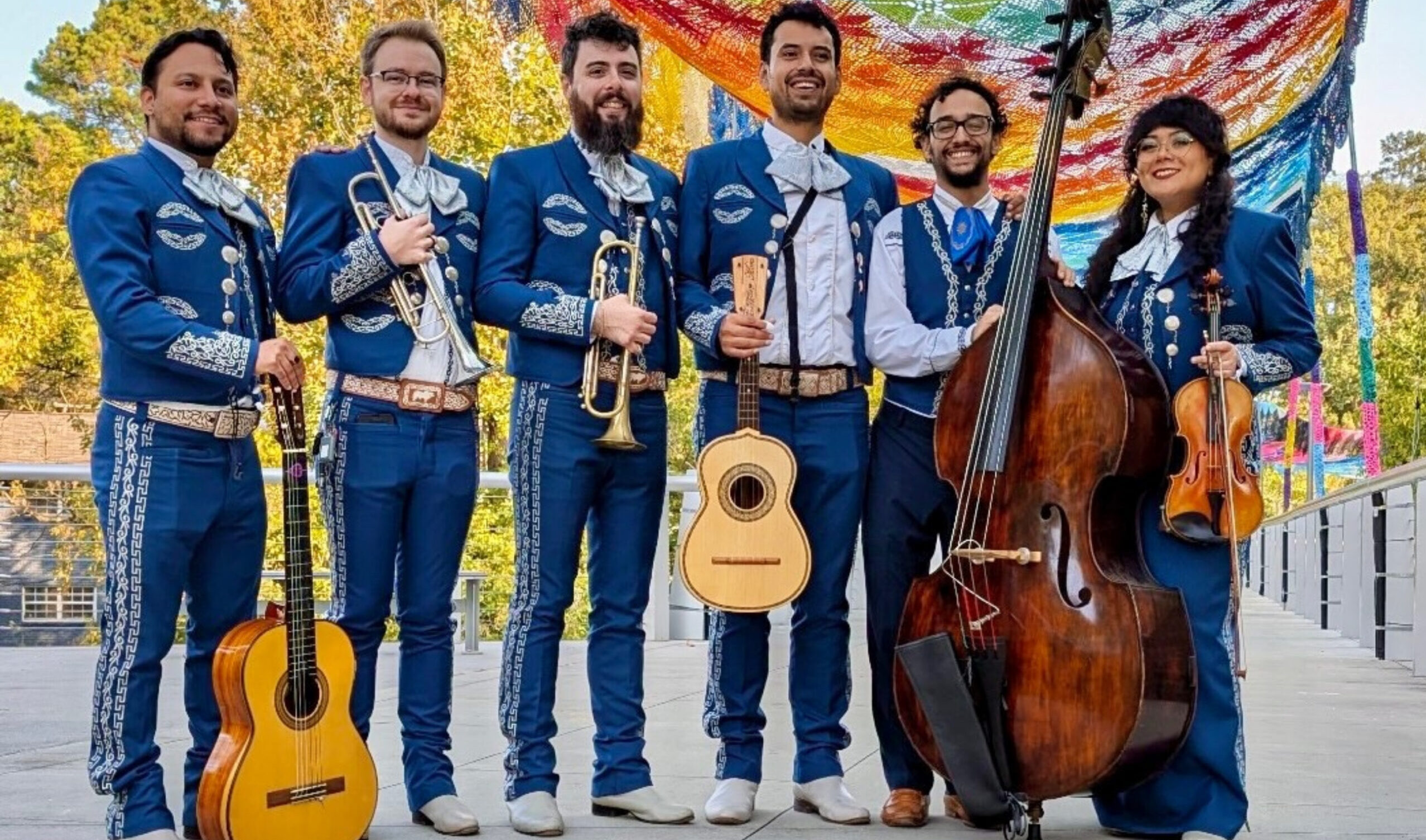 Photo of a six-person mariachi band in a line, facing the camera, and each holding a musical instrument