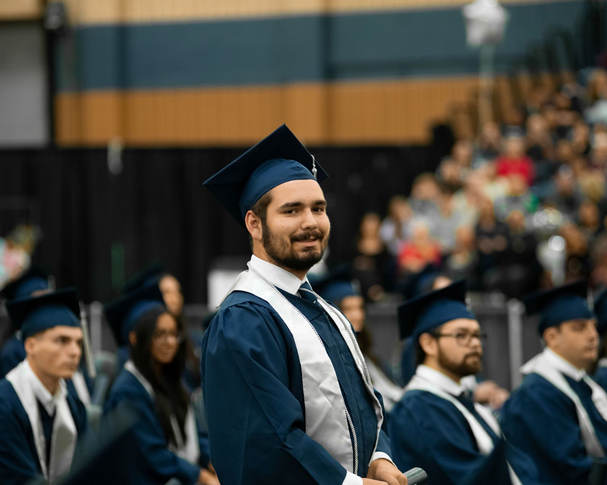 A graduate stands and looks at the camera during a commencement ceremony.