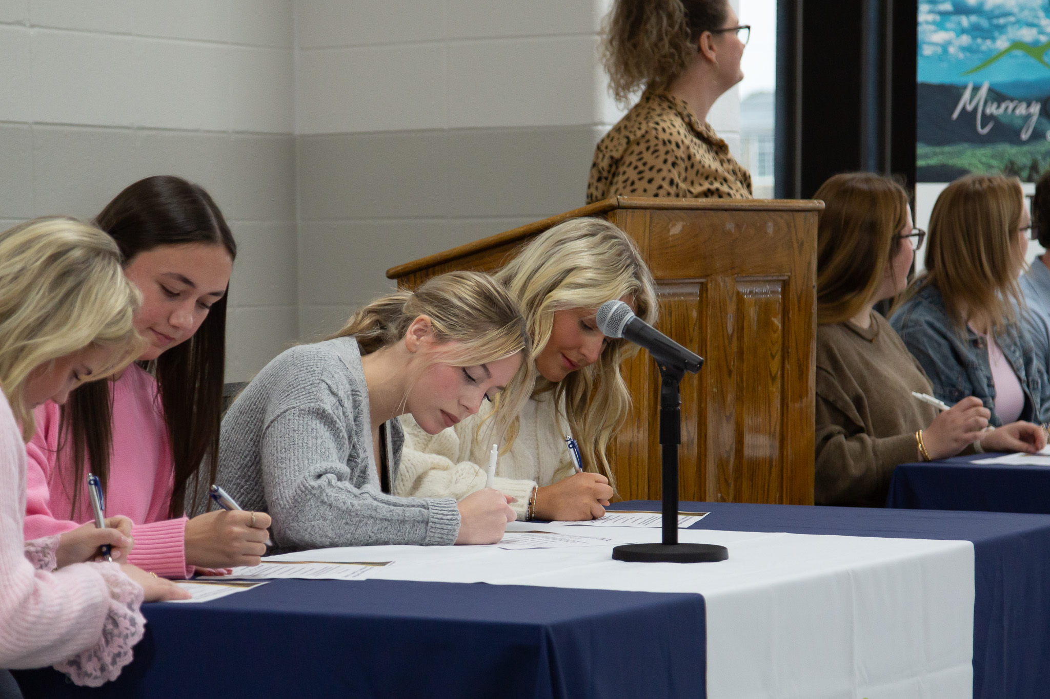 Students seated behind a table and sign a certificate.